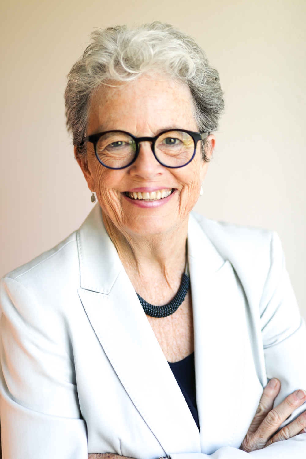 portrait photo of Trish Karlinski, wearing a white blazer, black sunglasses, and a black necklace